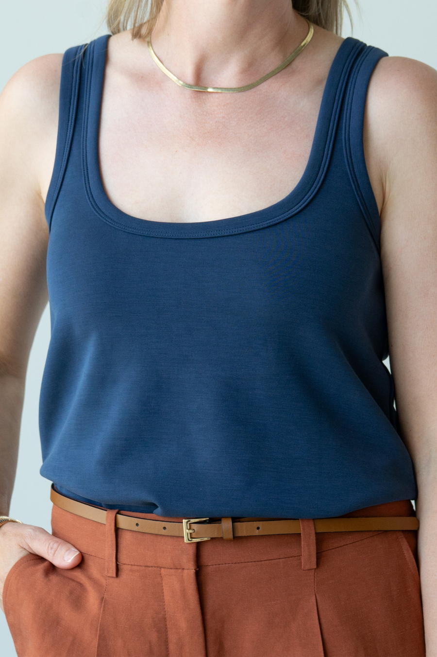 Person wearing a blue tank top and brown pants against a light gray background
