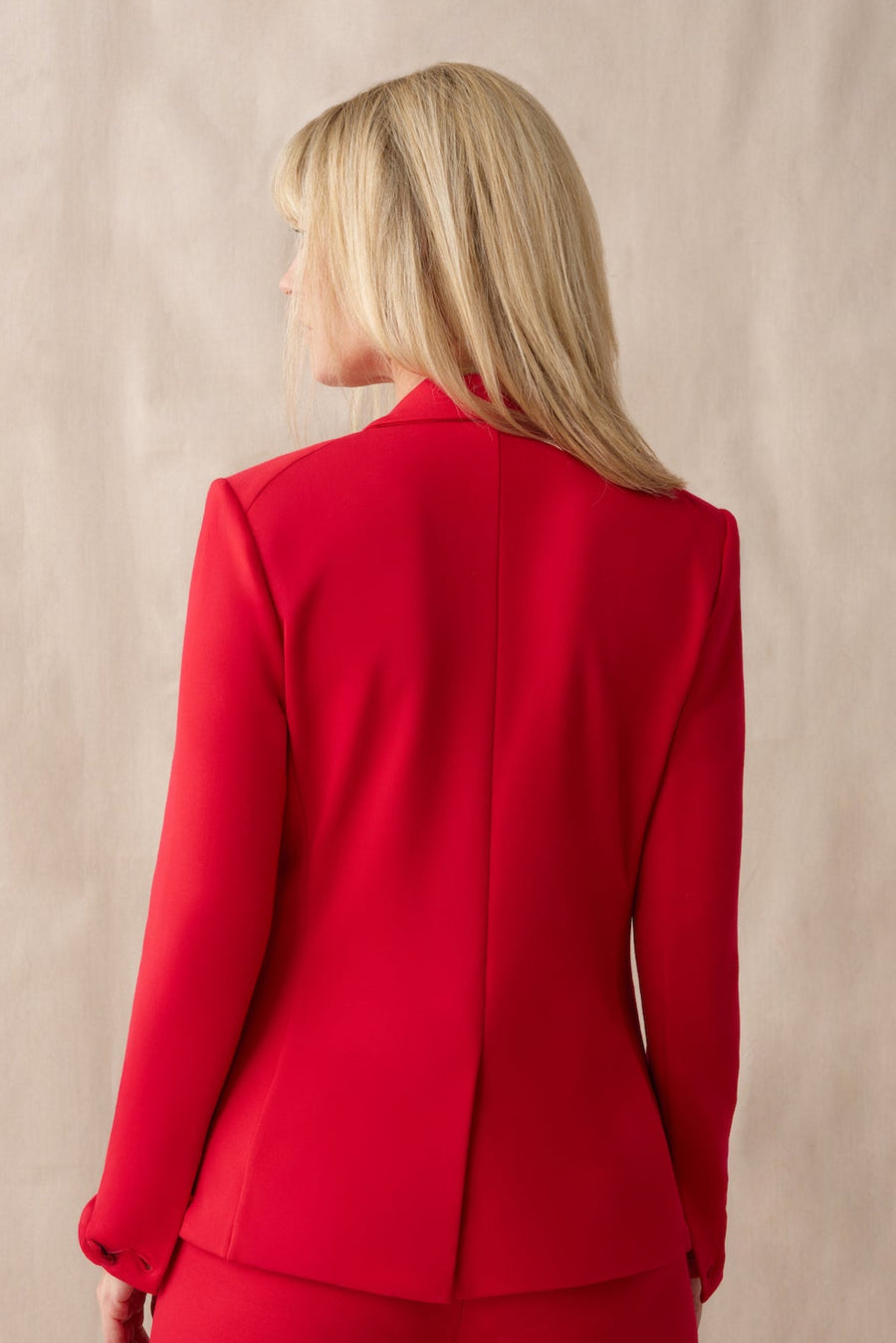 Person wearing a red suit standing against a beige background