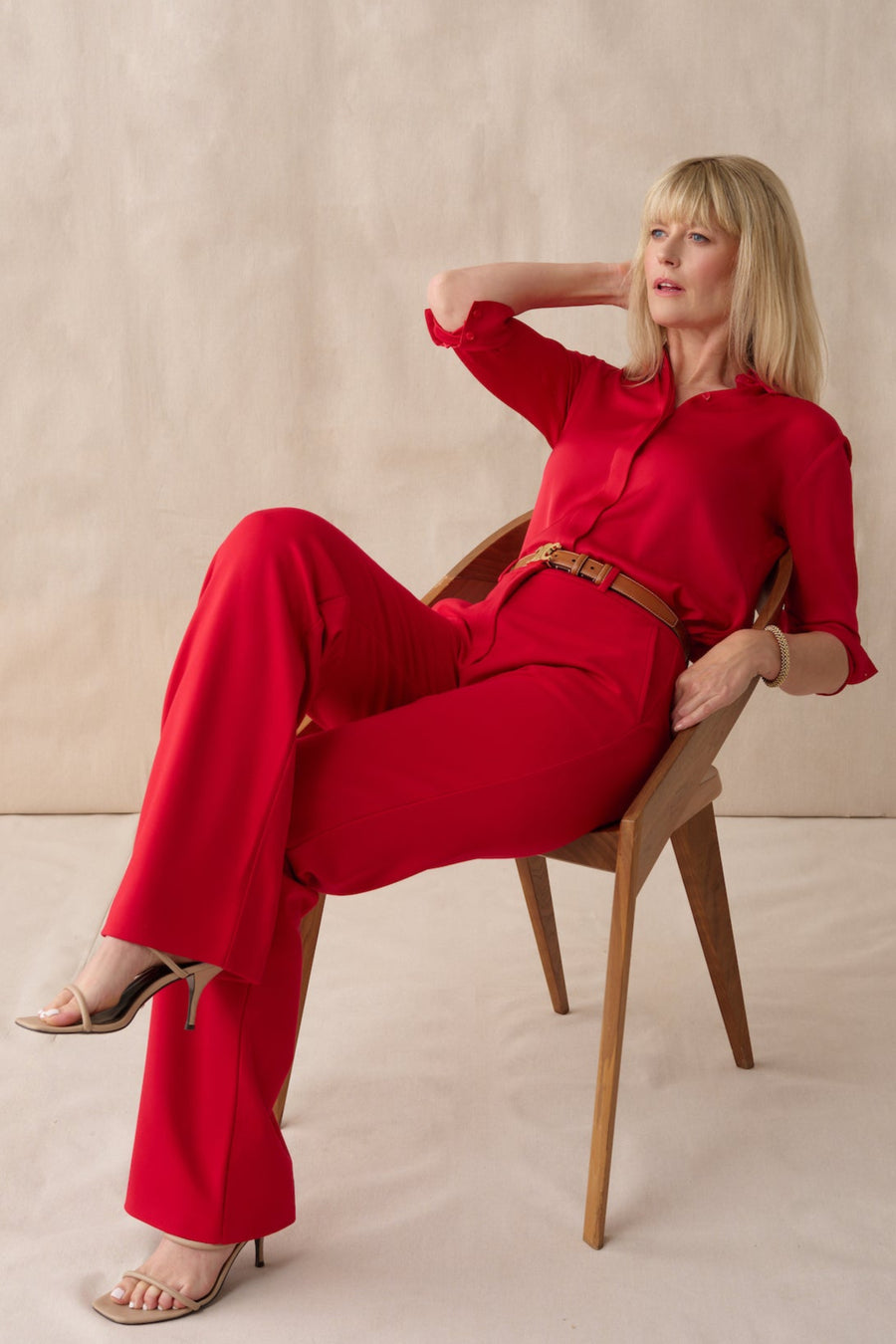 Woman in a red outfit sitting on a chair against a beige background