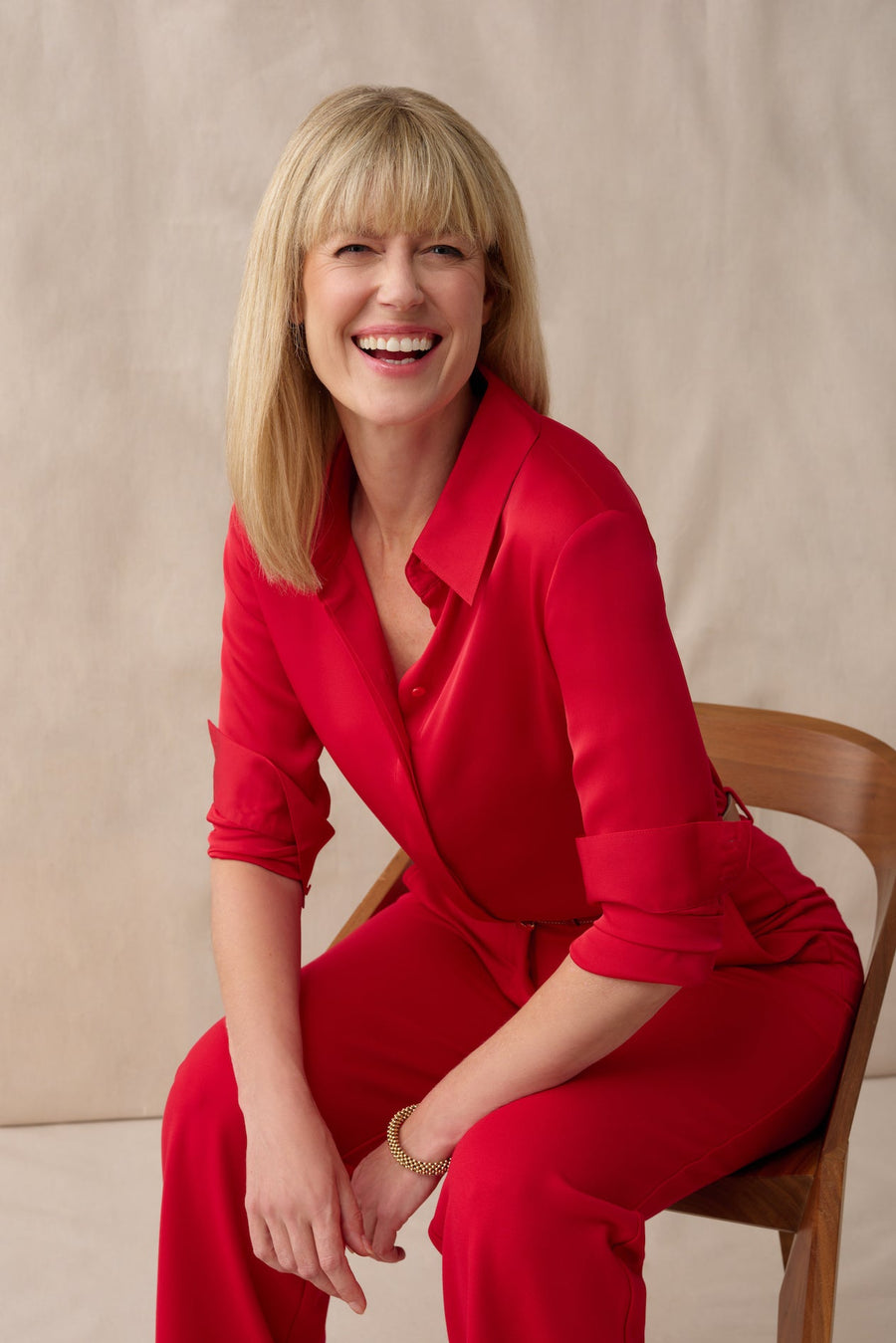 Woman in a red outfit sitting on a wooden chair against a beige background