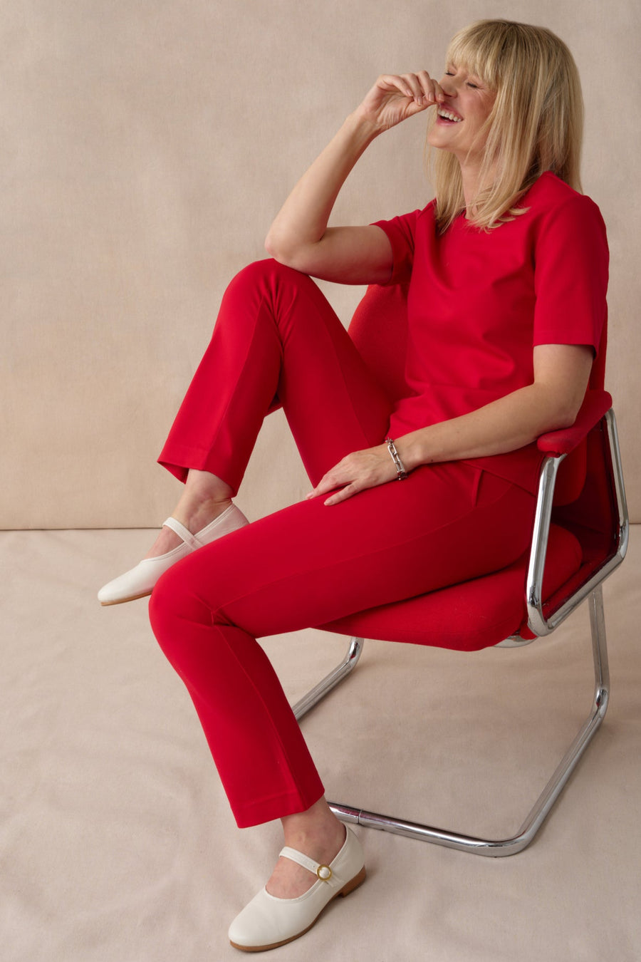 Woman in a red outfit sitting on a chair against a beige background