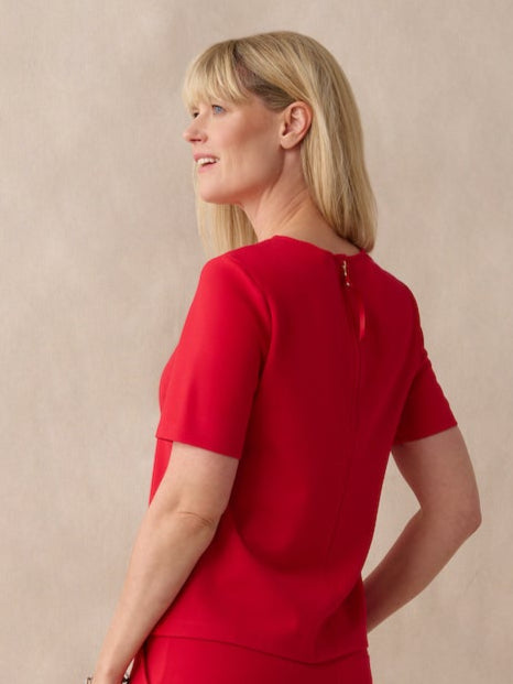 Woman wearing a red jumpsuit standing against a beige background