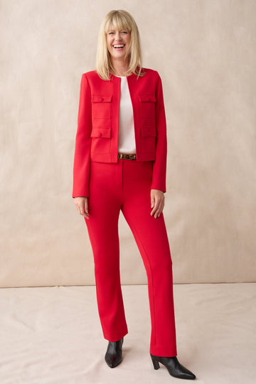 Woman wearing a red suit standing against a beige background