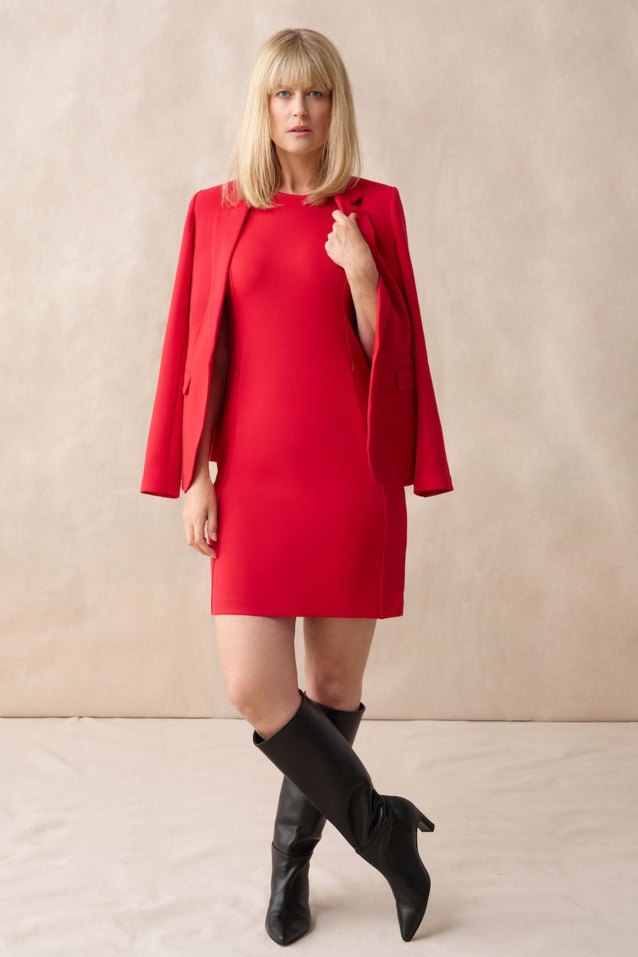 Woman wearing a red dress with a matching jacket and black boots on a beige background