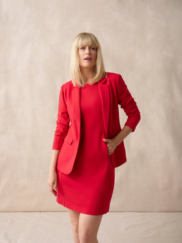 Woman wearing a red dress and jacket set against a beige background