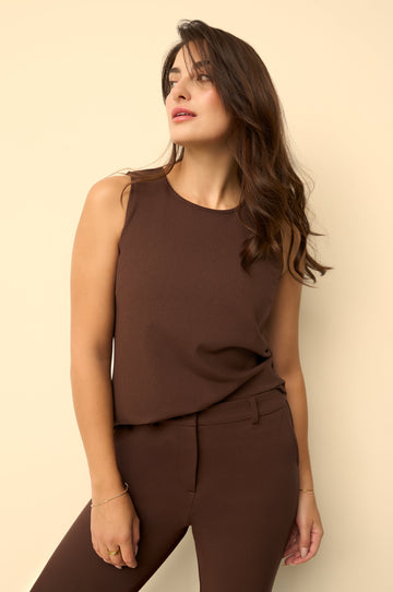 Woman wearing a brown sleeveless top and pants against a beige background