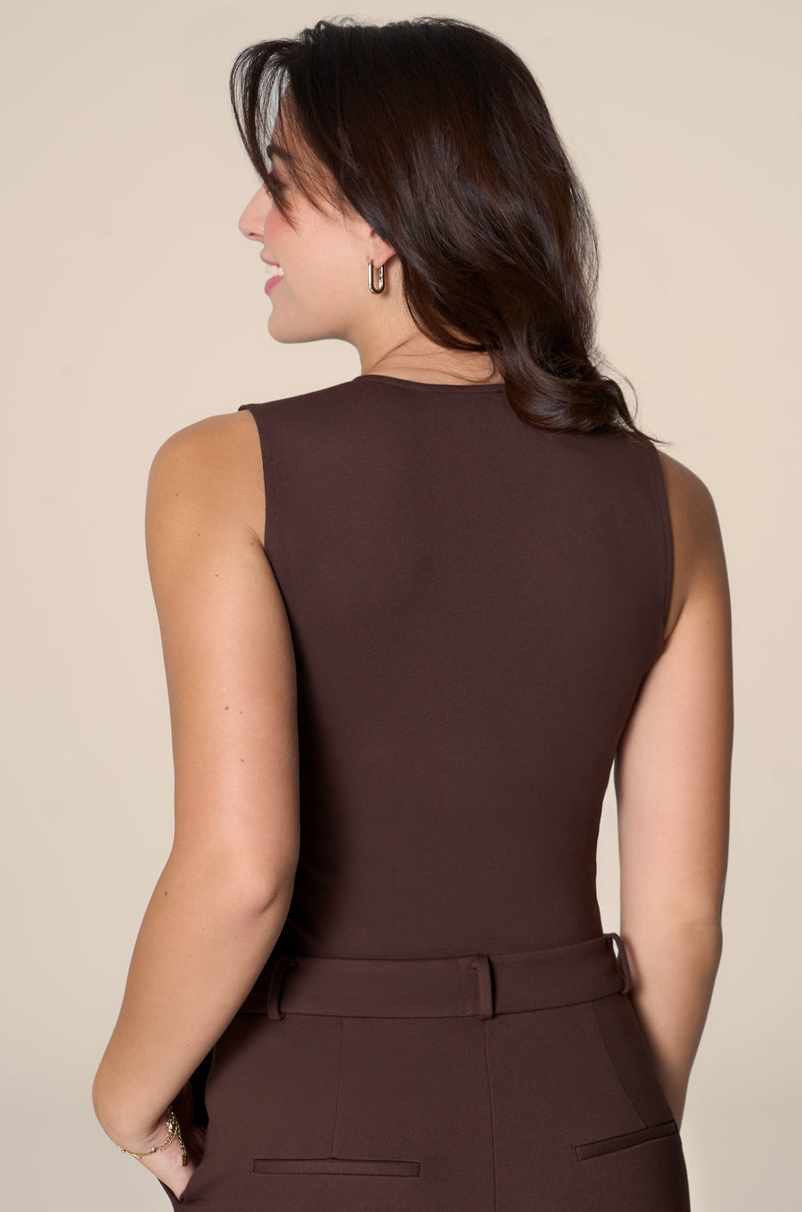 Woman wearing a brown sleeveless top and pants against a beige background