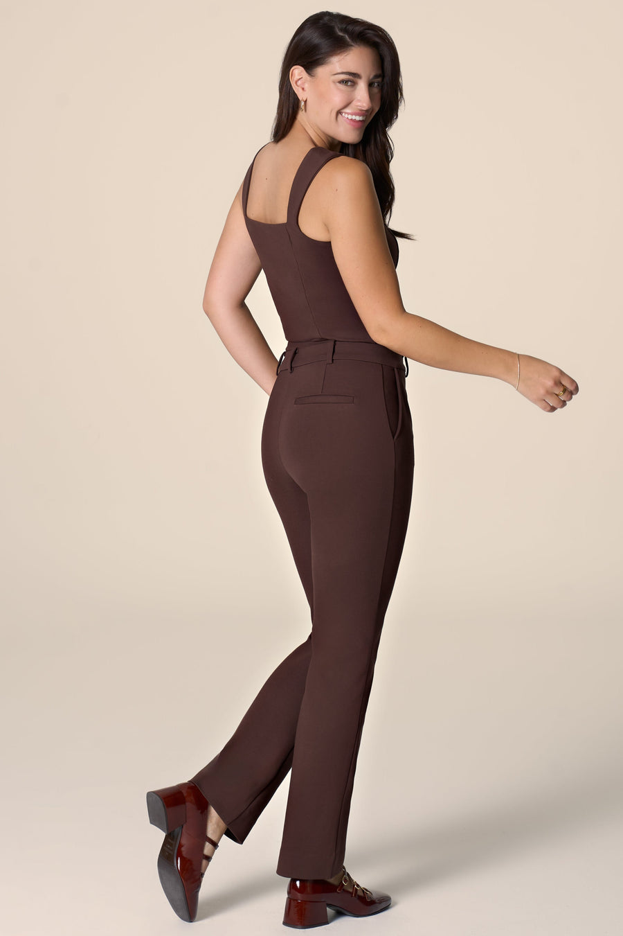 Woman in a brown pants and matching top sitting against a plain background