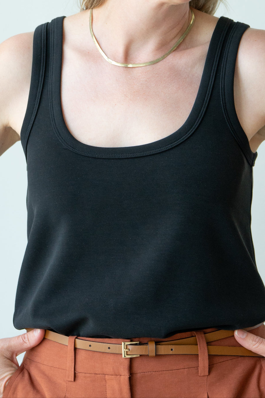 Person wearing a black tank top and brown pants with a plain background