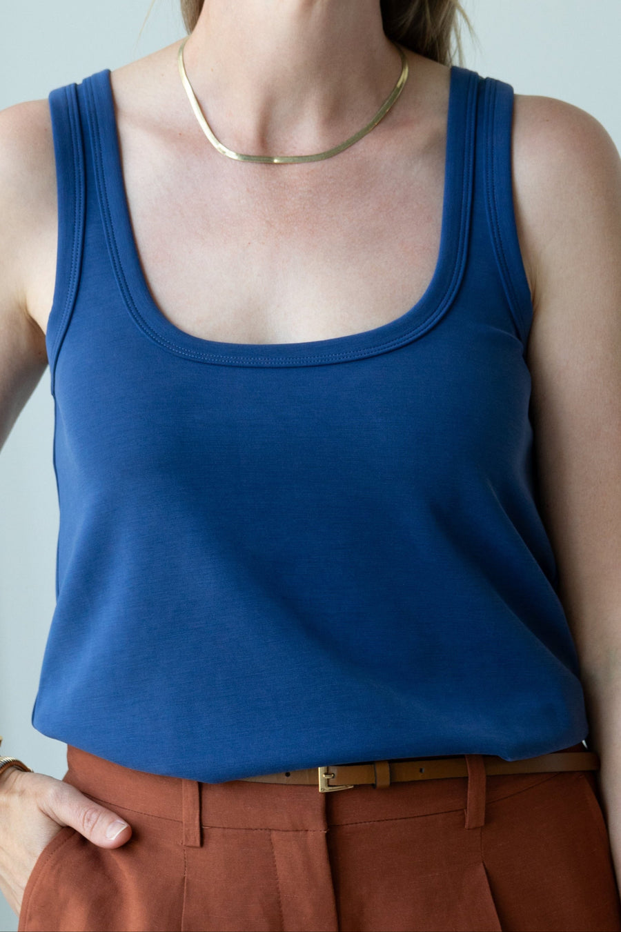Person wearing a blue tank top and brown pants against a light gray background