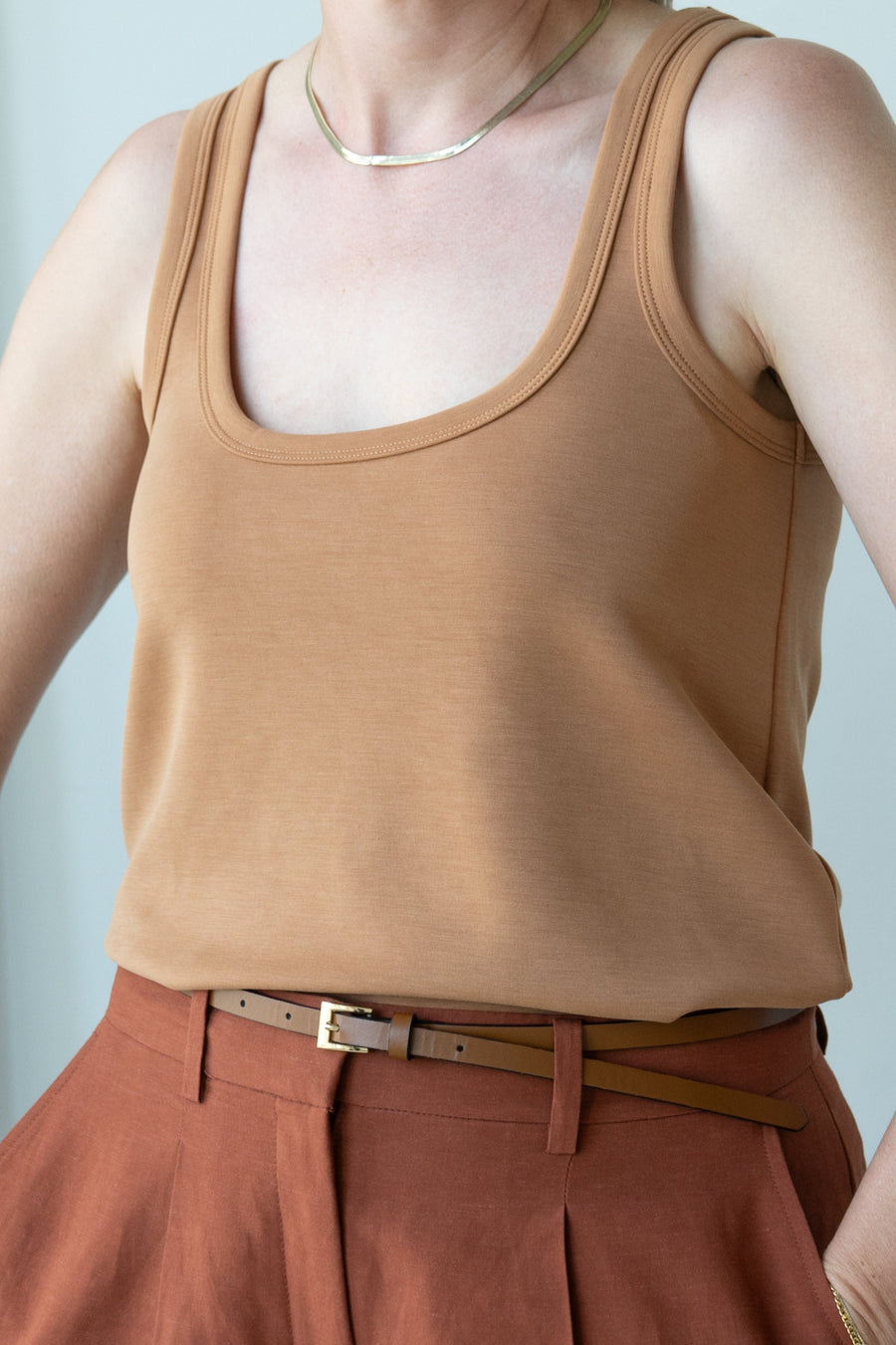 Person wearing a brown tank top and pants against a light background