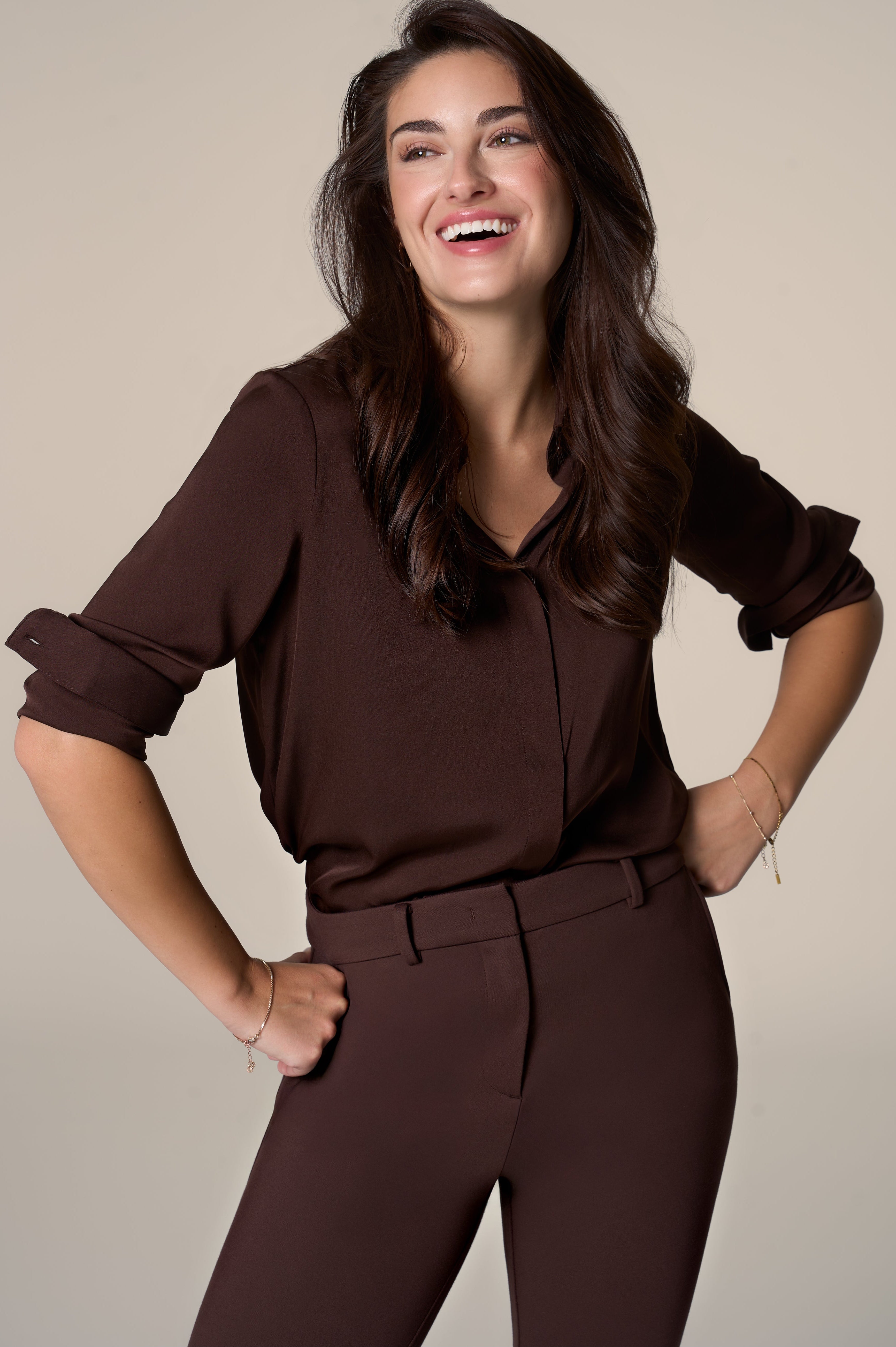 Woman wearing a brown silk blouse and matching pants against a beige background