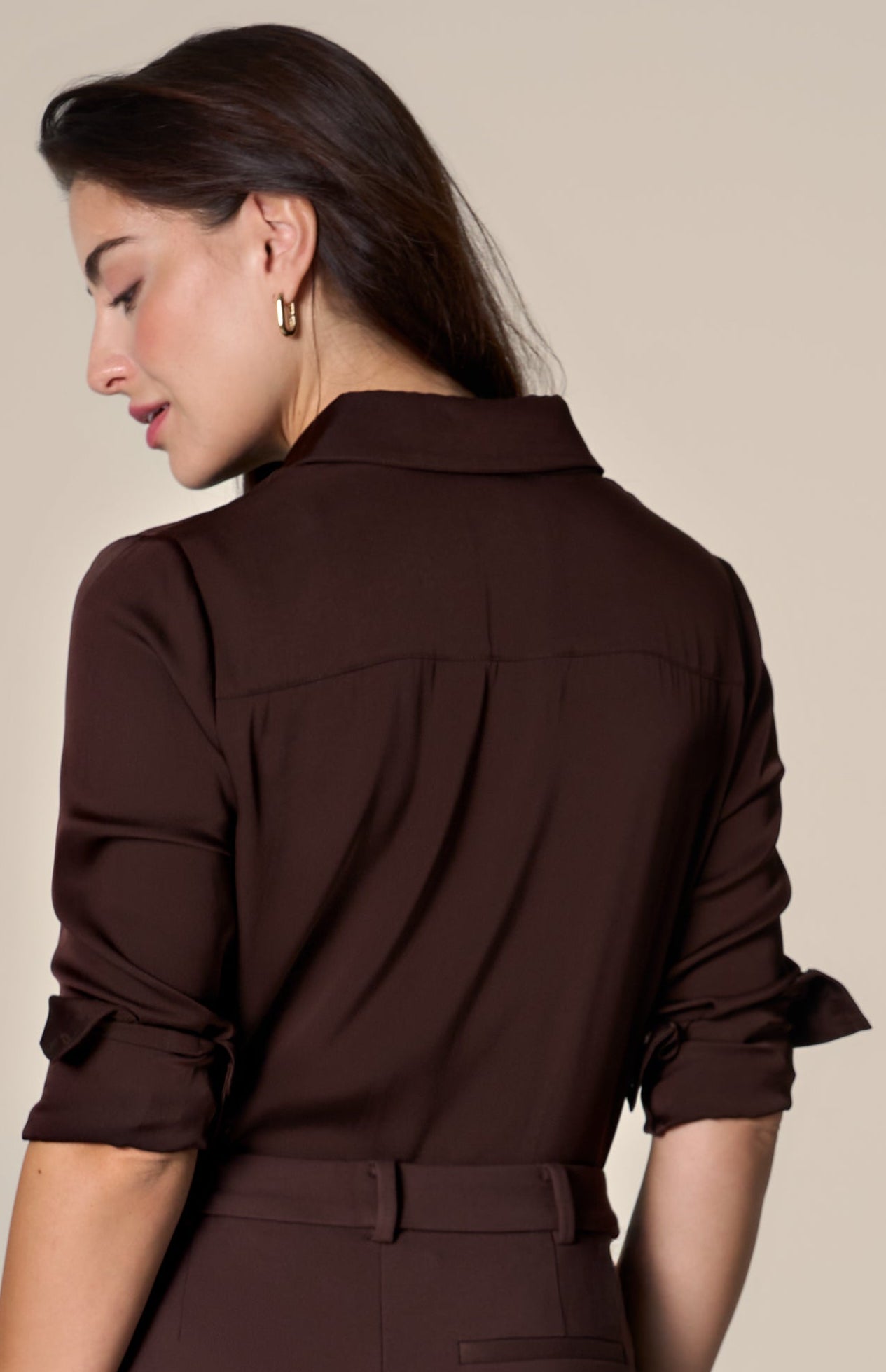 Woman wearing a brown silk blouse and matching pants against a beige background