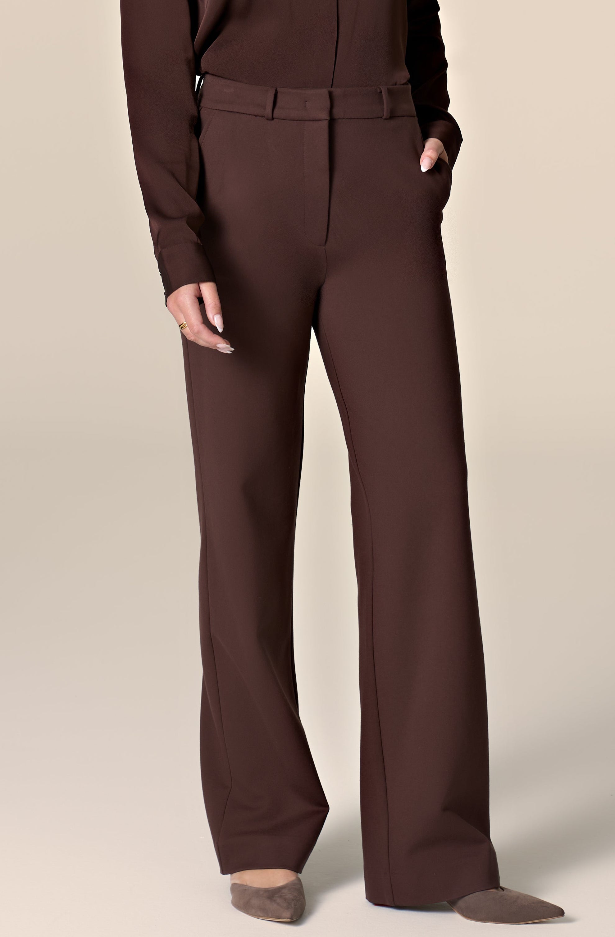 Woman wearing brown silk blouse and tailored work pants in front of a plain background.