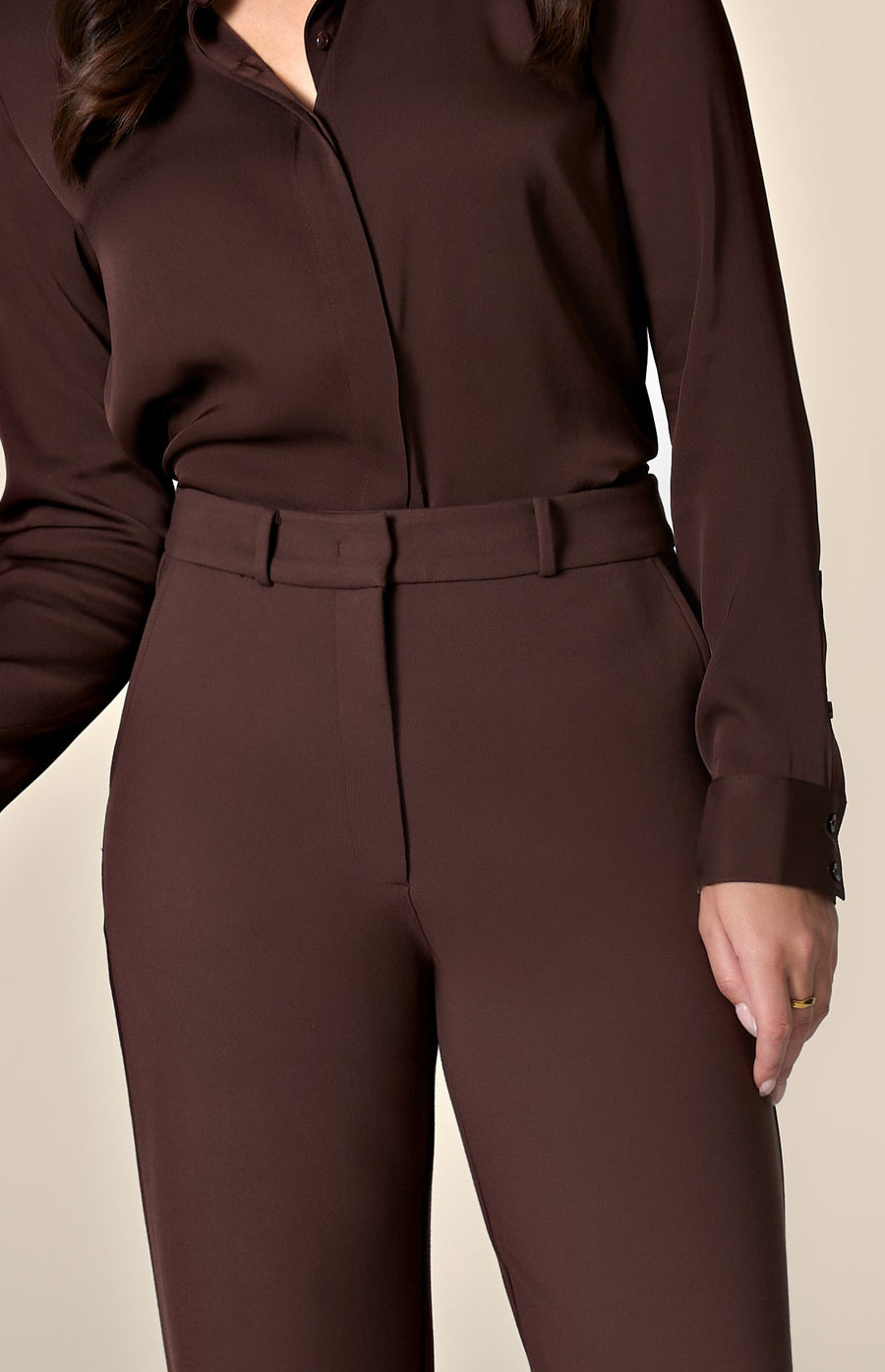 Woman wearing brown silk blouse and tailored work pants in front of a plain background.