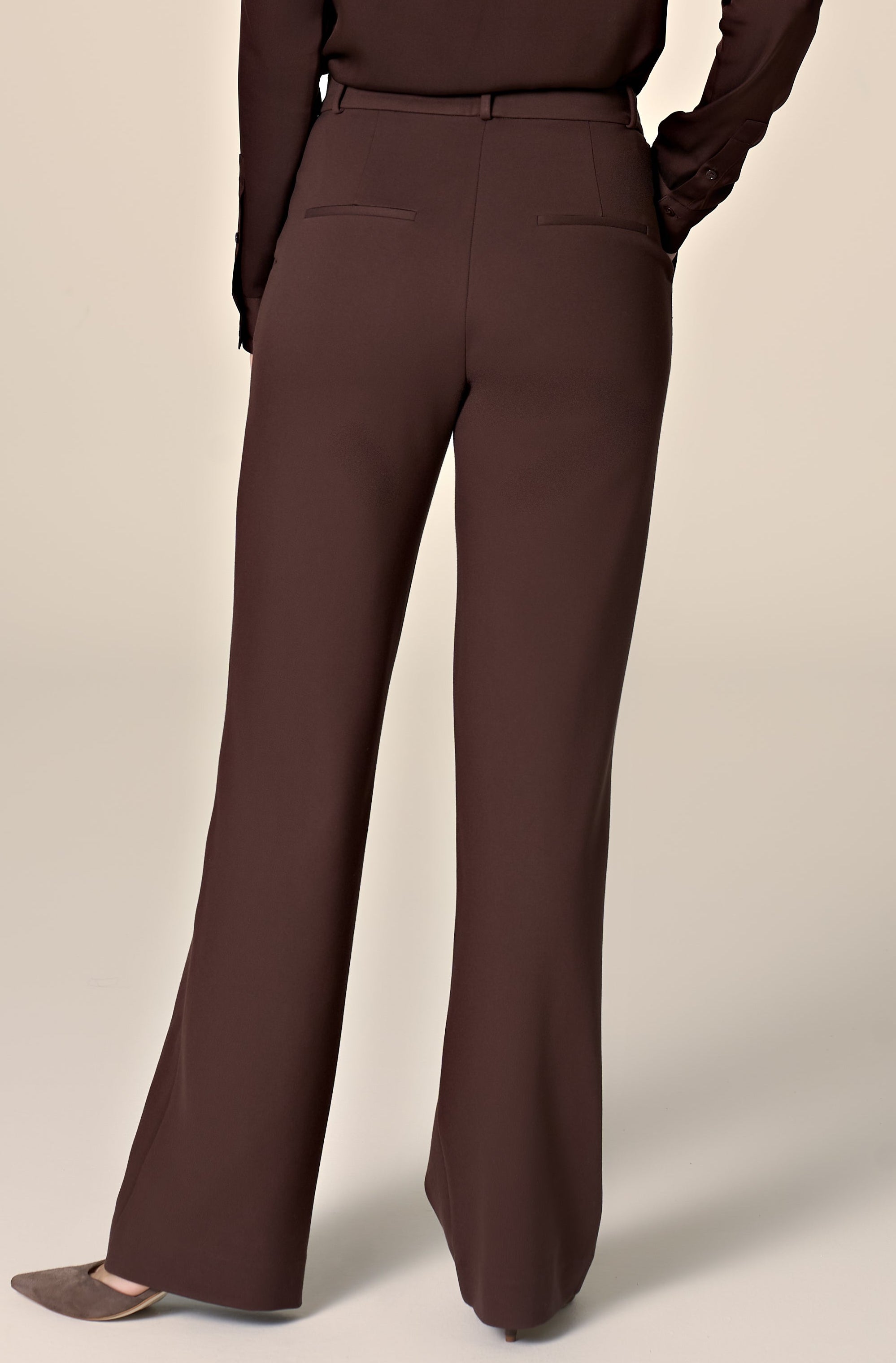 Woman wearing brown silk blouse and tailored work pants in front of a plain background.