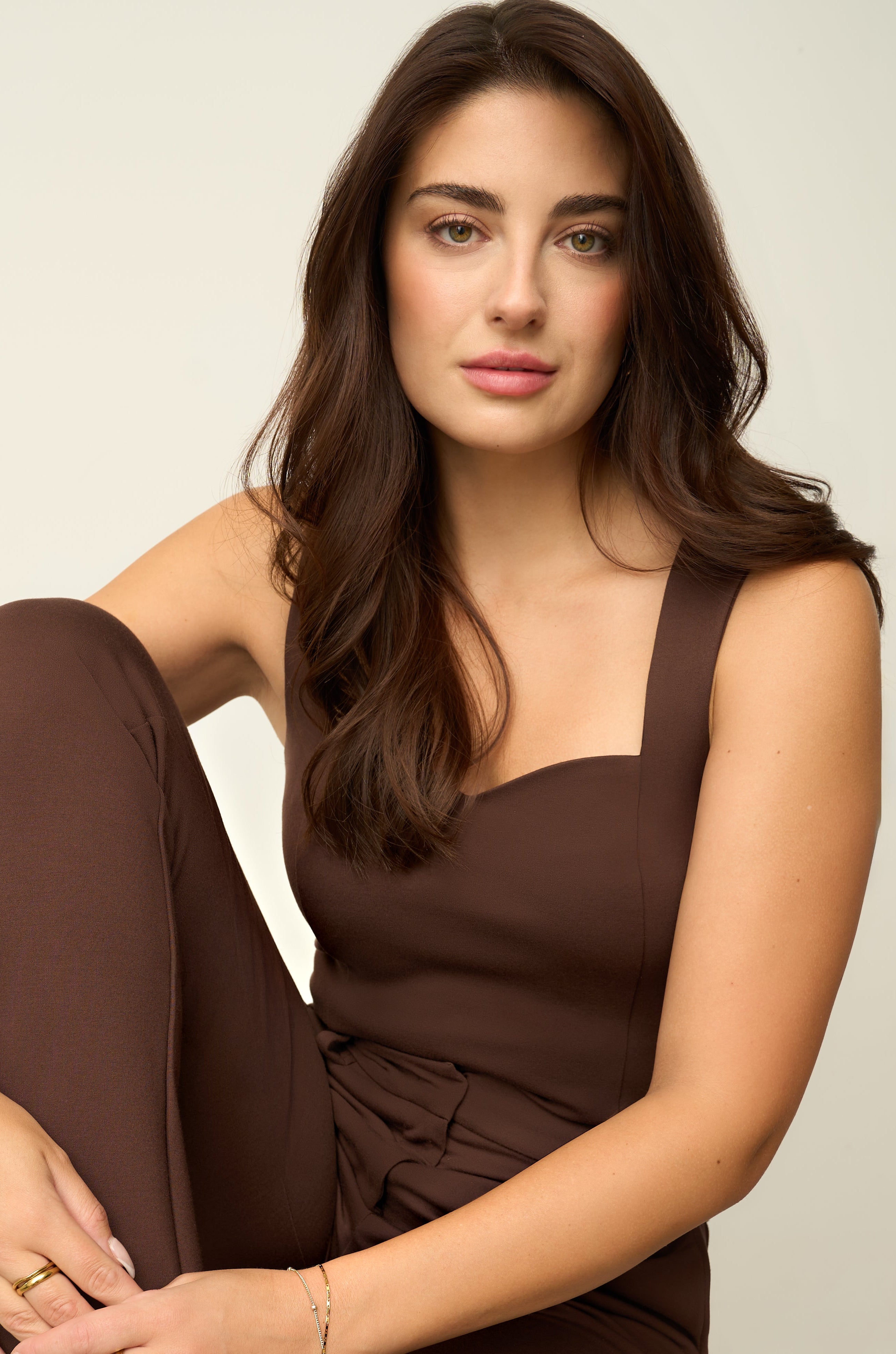 Woman wearing a brown jumpsuit sitting on a white surface.